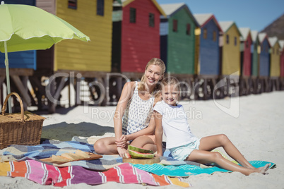Portrait of smiling woman with her daughter sitting on blanket at beach