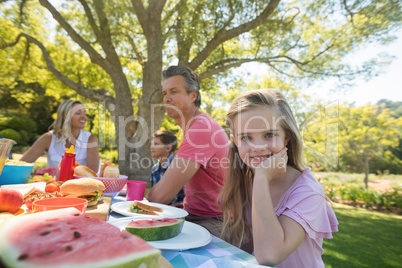 Girl sitting at the table with having meal whith her family in park