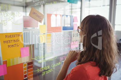 Businesswoman planning with adhesive notes on glass in office