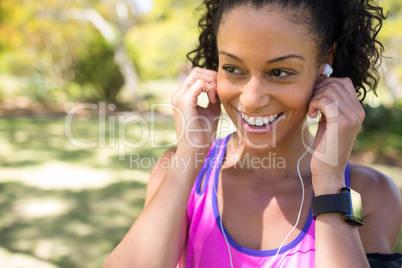 Smiling jogger woman adjusting her headphones in the park