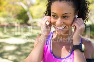 Smiling jogger woman adjusting her headphones in the park