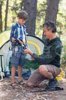 Father offering hiking poles to son in forest