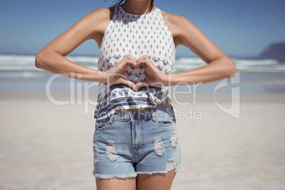 Mid section of woman making heart shape with hands at beach