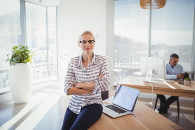 Portrait of confident executive sitting with arms crossed on desk