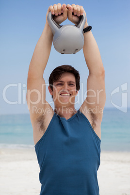 Happy young man lifting kettlebell at beach