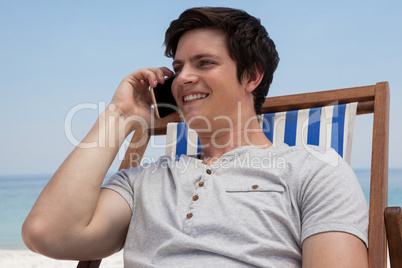 Man sitting on sunlounger and talking on mobile phone on the beach