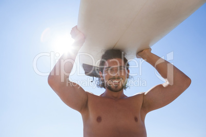 Surfer carrying surfboard over head against blue sky