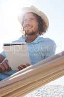 Man relaxing on hammock and using digital tablet on the beach