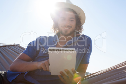 Smiling man using digital tablet on hammock at beach