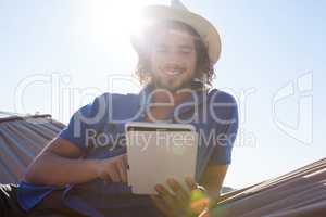 Smiling man using digital tablet on hammock at beach