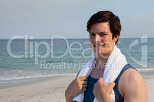 Smiling man standing on beach with towel around his neck