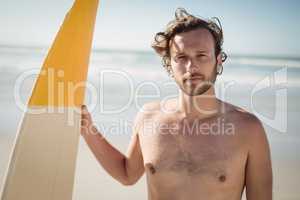 Portrait of shirtless man holding surfboard at beach