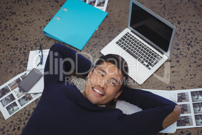 Smiling businessman lying by laptop and photographs at office