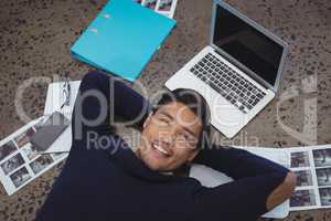 Smiling businessman lying by laptop and photographs at office