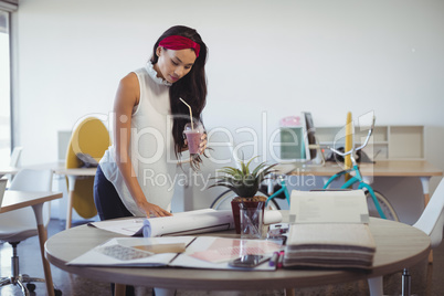 Businesswoman holding drink while working at office desk
