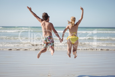 Rear view of couple holding hands while jumping at beach