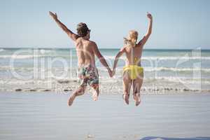 Rear view of couple holding hands while jumping at beach