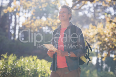 Happy male hiker standing with digital tablet in forest