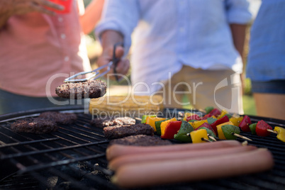 Family grilling patties, vegetables and sausages on the barbecue grill