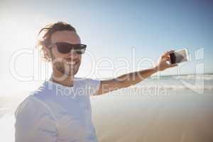 Portrait of smiling man taking selfie against clear sky at beach