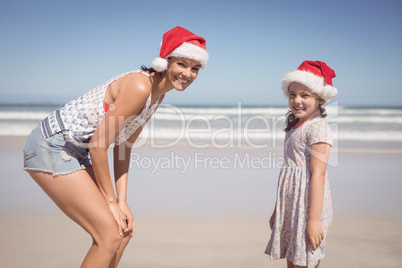 Portrait of happy woman with daughter wearing Santa hat at beach