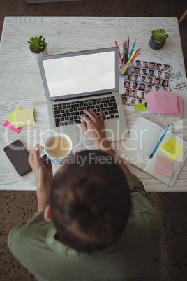 Female photo editor holding coffee cup while using laptop in office