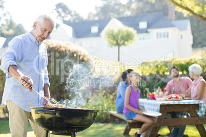 Senior man preparing barbecue while family having meal