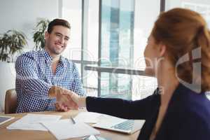 Smiling executives shaking hands at desk