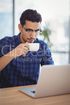 Attentive executive having coffee while using laptop at desk