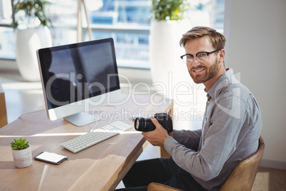 Portrait of smiling executive holding digital camera at desk