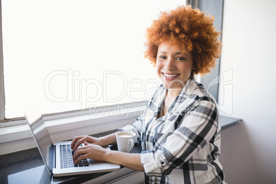 Portrait of smiling businesswoman using laptop on window sill