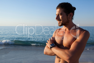Muscular man standing with arms crossed at beach