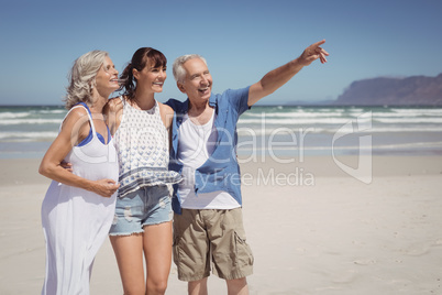 Happy senior man pointing away while standing with family at beach