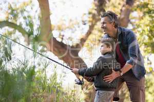 Smiling father assisting son while fishing in forest