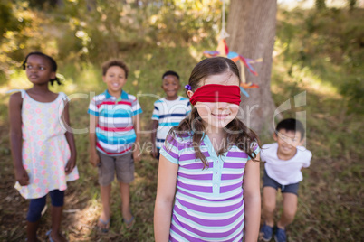 Friends looking at blindfolded girl standing in forest