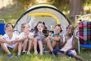 Happy friends holding candies by tent at campsite