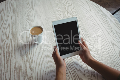 Hands of woman holding holding digital tablet by coffee cup on table