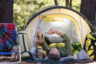 Father and son using digital tablet while relaxing at campsite