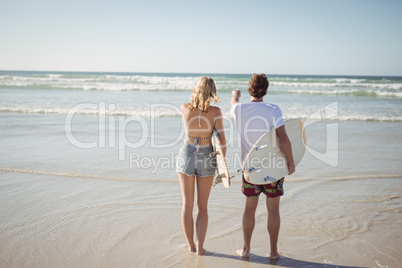 Rear view of couple holding surfboards while standing at beach