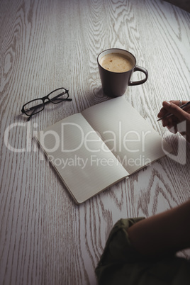 Businesswoman writing on book at office desk