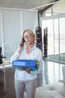 Businesswoman talking on mobile phone while holding files