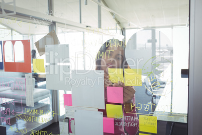 Businesswoman seen through adhesive notes on glass in creative office