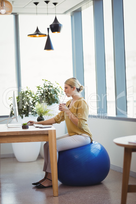 Executive sitting on fitness ball while working at desk