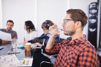 Businessman drinking water while sitting with colleagues