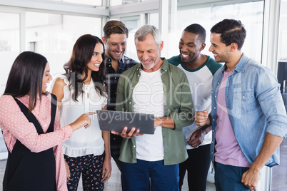 Happy colleagues looking at laptop held by businessman
