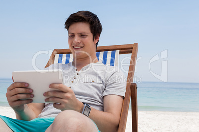 Man sitting on sunlounger and using digital tablet on the beach