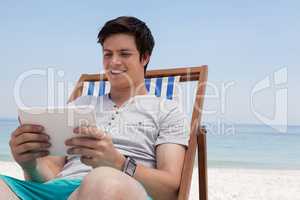Man sitting on sunlounger and using digital tablet on the beach