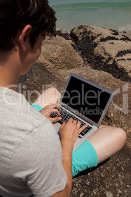 Man sitting on the rocks and using laptop at the sea coast