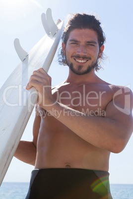 Smiling surfer with surfboard standing at beach coast