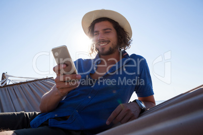 Smiling man using mobile phone while relaxing on hammock at beach